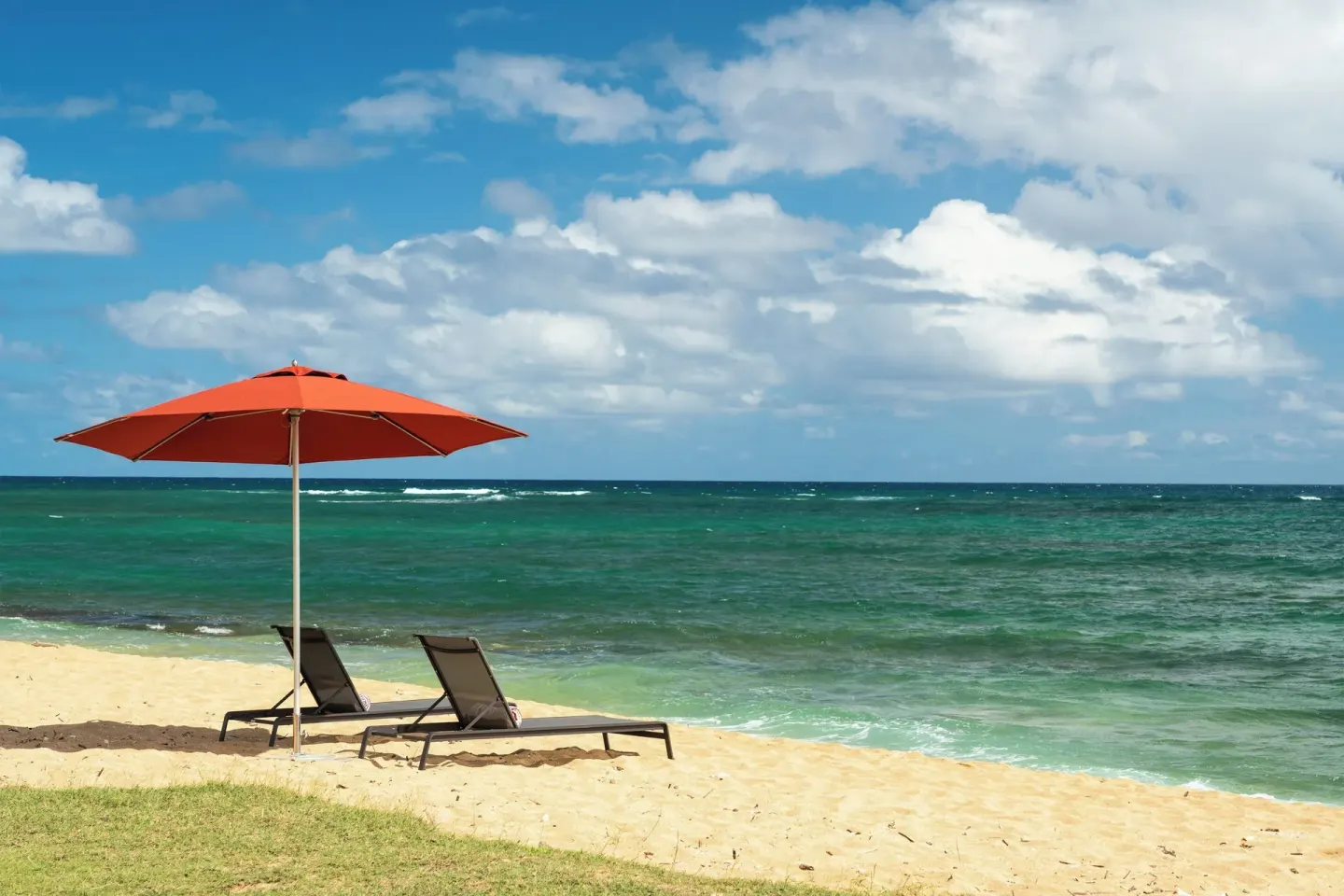 Beach loungers and a red umbrella face the ocean at Sheraton Kauai Coconut Beach Resort.