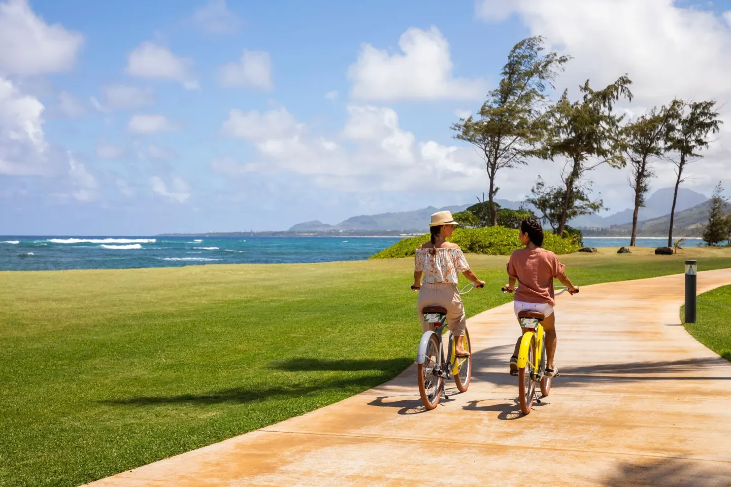 Two cyclists ride away along the oceanfront path at Sheraton Kauai Coconut Beach Resort.