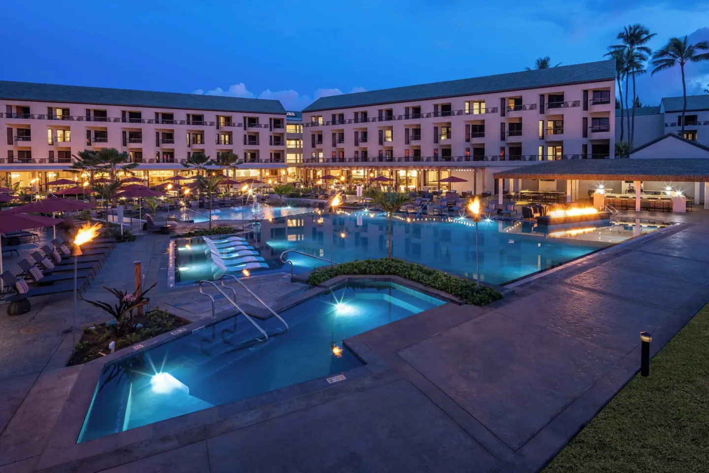 Evening pool courtyard at Sheraton Kauai Coconut Beach Resort with lit guest room buildings.