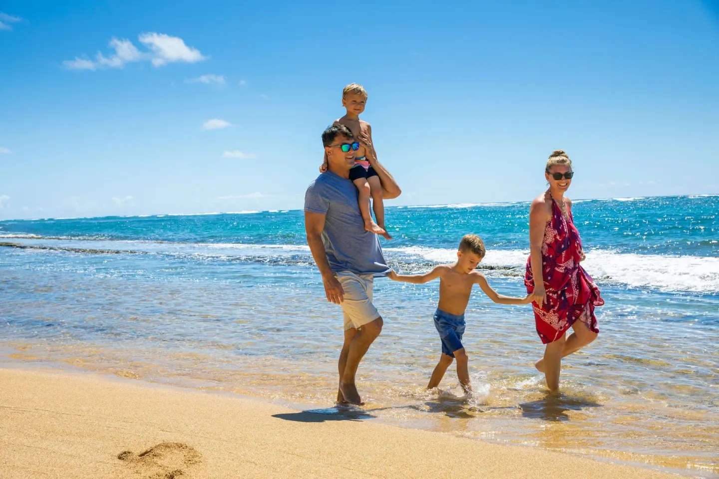 A family walks in shallow surf by the beach at Sheraton Kauai Coconut Beach Resort.
