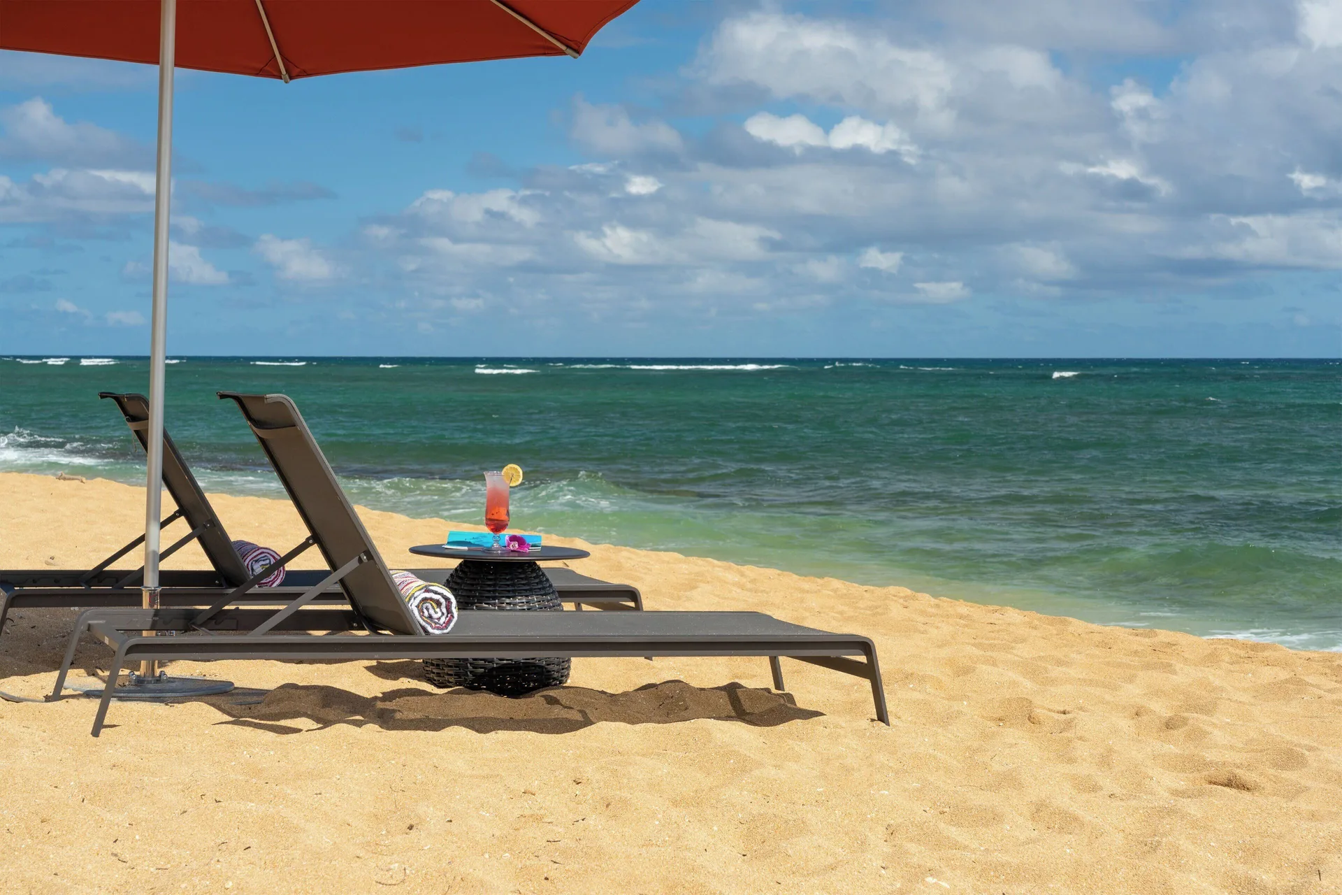 Oceanfront beach loungers with a drink on a table at Sheraton Kauai Coconut Beach Resort.
