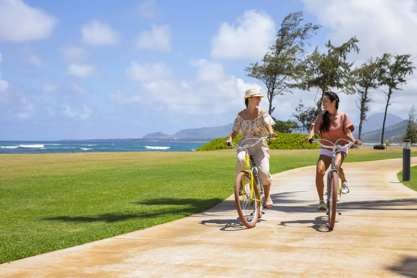 Two guests ride bicycles by the oceanfront lawn at Sheraton Kauai Coconut Beach Resort.