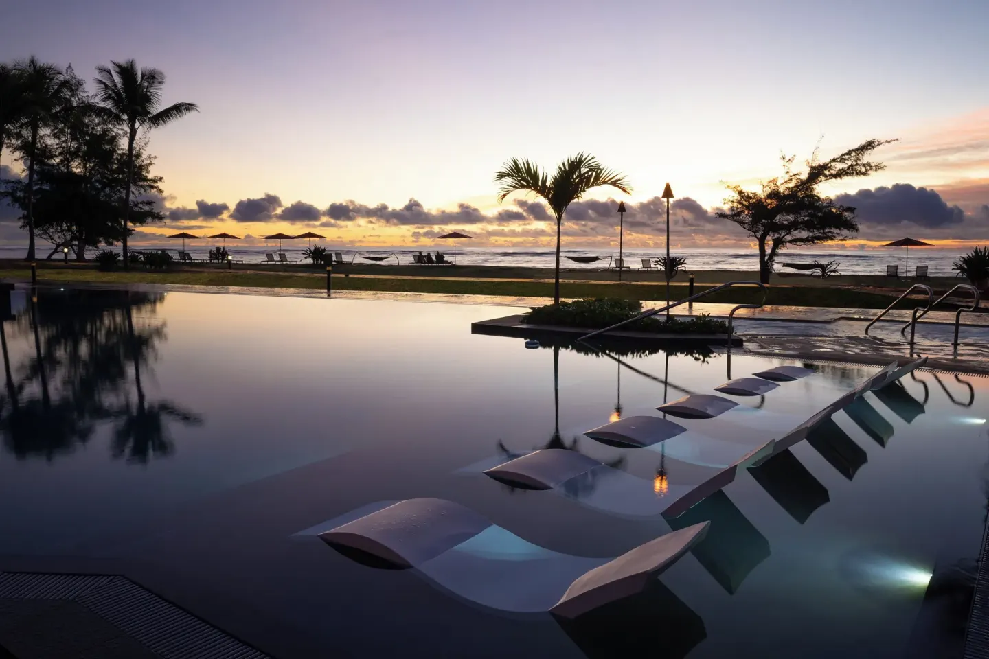 Infinity pool at Sheraton Kauai Coconut Beach Resort with in-water loungers at sunrise.