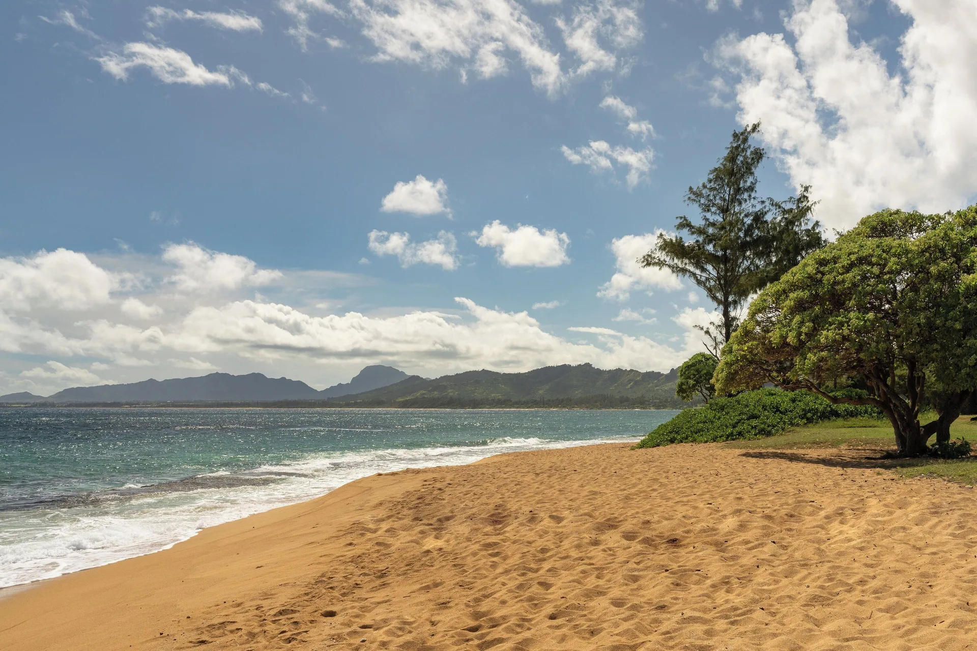 Sandy beach with ocean waves and distant mountains at Sheraton Kauai Coconut Beach Resort.