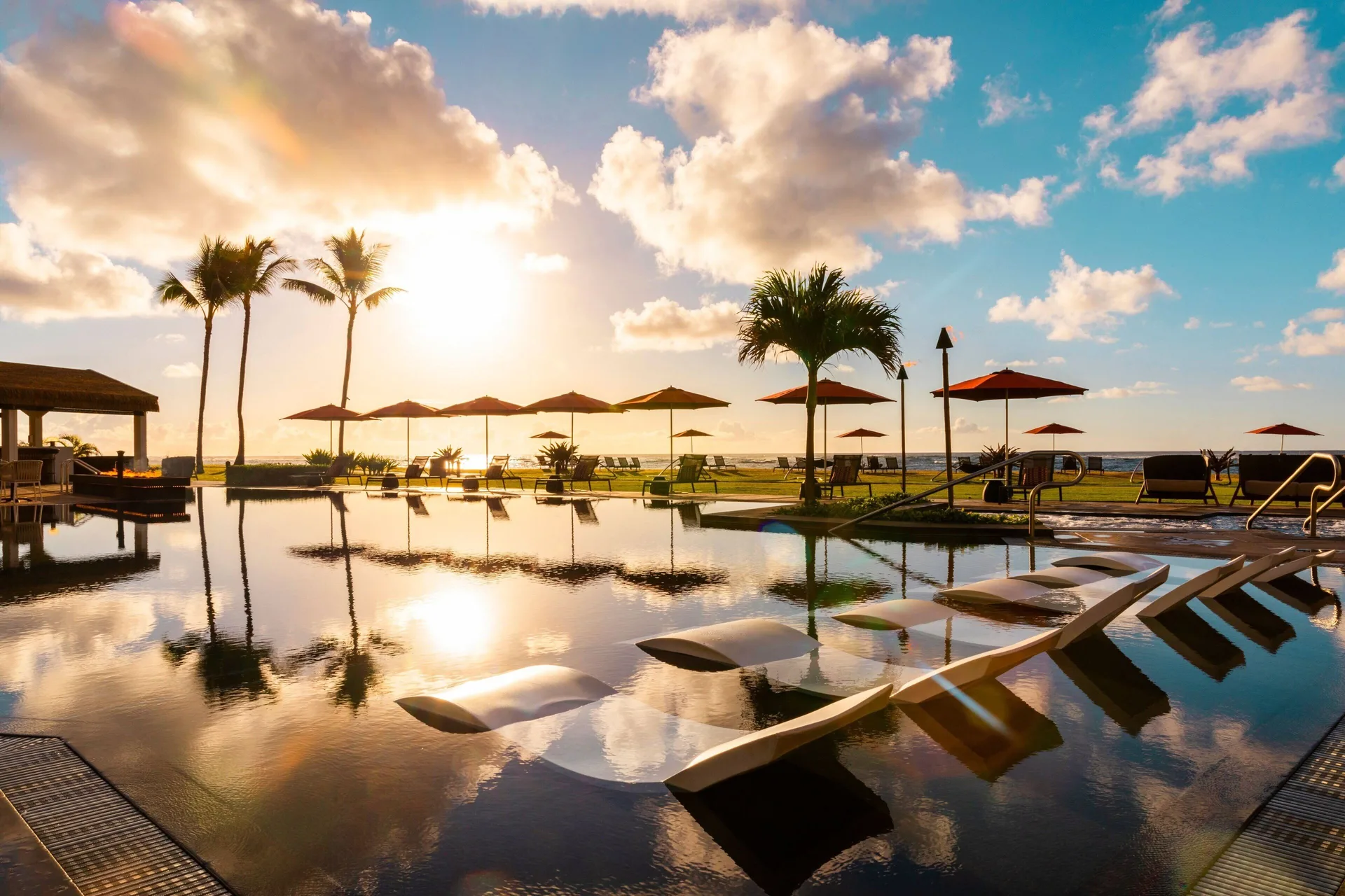 Sunlit infinity pool at Sheraton Kauai Coconut Beach Resort with loungers and ocean beyond.