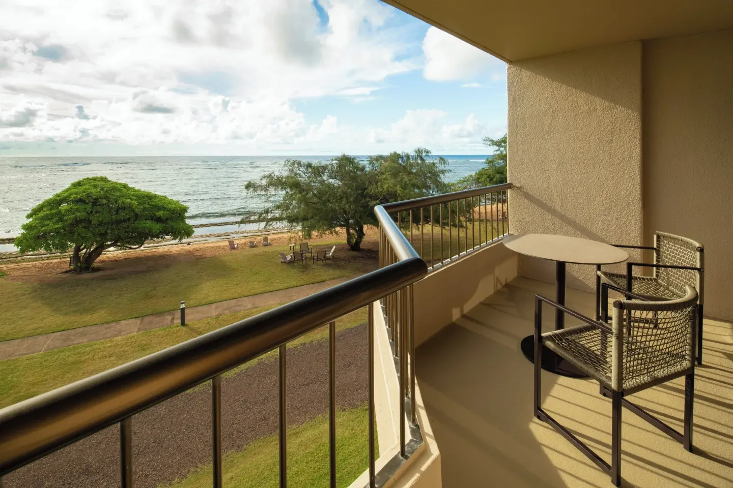 Ocean View room balcony with table, chair, lawn, trees, and ocean at Sheraton Kauai Coconut Beach Resort.