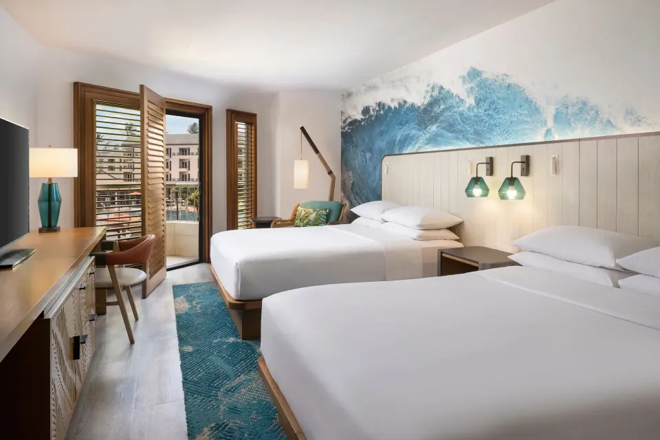 Guest room with two beds, balcony door, and wave mural at Sheraton Kauai Coconut Beach Resort.