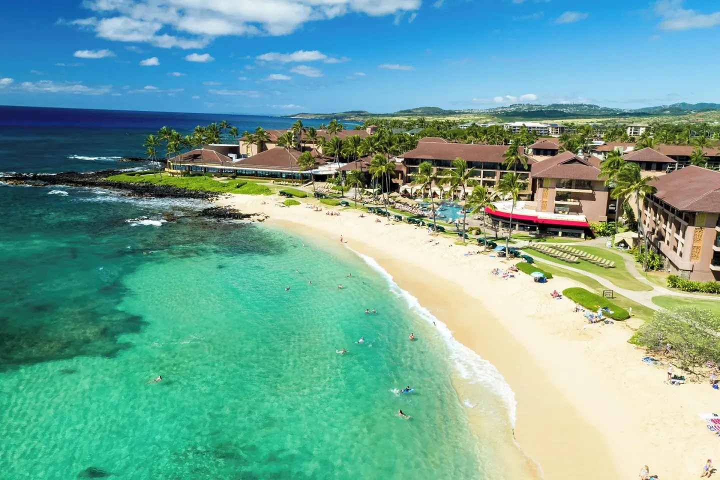 Aerial view of Sheraton Kauai Resort with beach, pool, palms, and clear turquoise water.