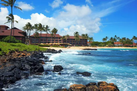Beachfront buildings at Sheraton Kauai Resort overlook turquoise water and black lava rocks.