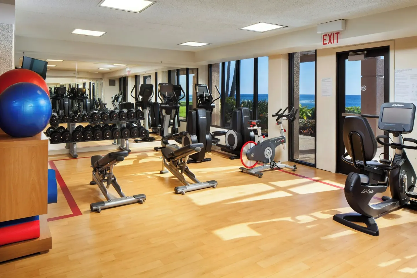 Fitness room with cardio machines, weights, and ocean-facing windows at Sheraton Kauai Resort.