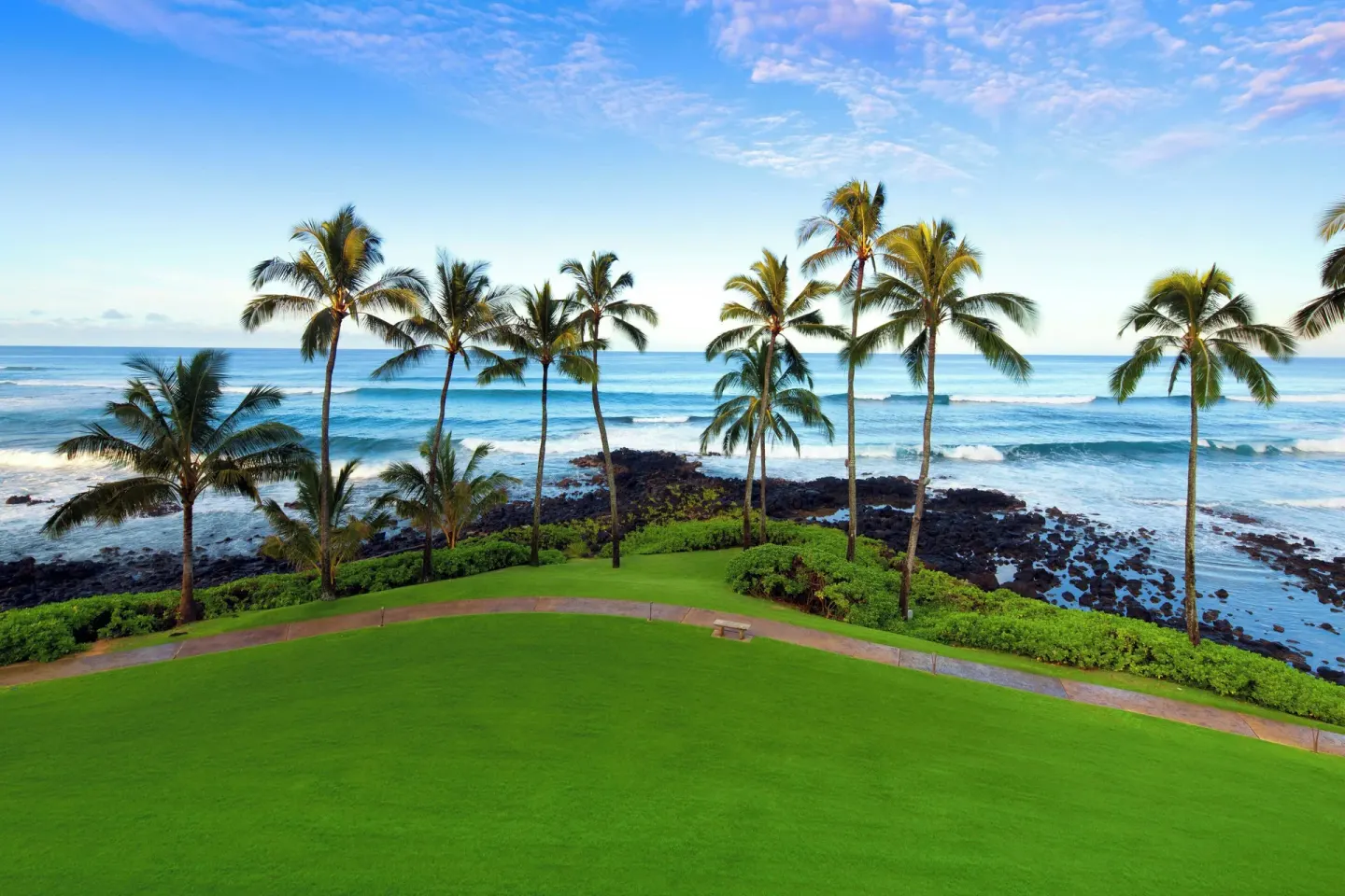 Green lawn and palm trees overlook the rocky oceanfront at Sheraton Kauai Resort.