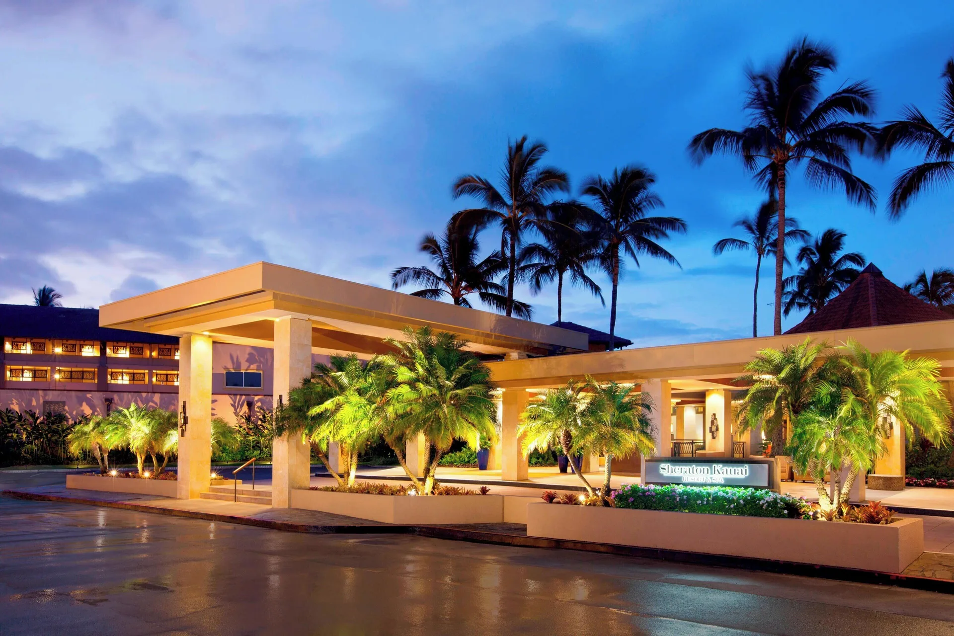 Illuminated porte cochere and palm trees at Sheraton Kauai Resort at dusk.