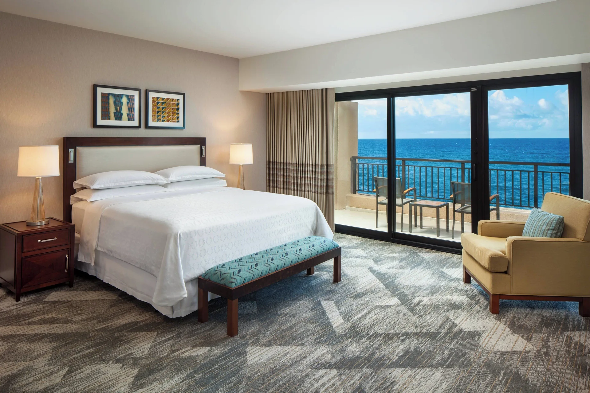 Oceanfront deluxe suite bedroom with king bed and balcony at Sheraton Kauai Resort.