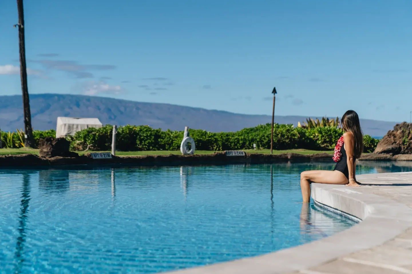 Guest sitting at the pool edge with ocean and island views at Sheraton Maui Resort & Spa.