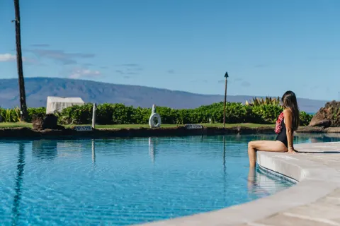 Guest sitting at the pool edge with ocean and island views at Sheraton Maui Resort & Spa.