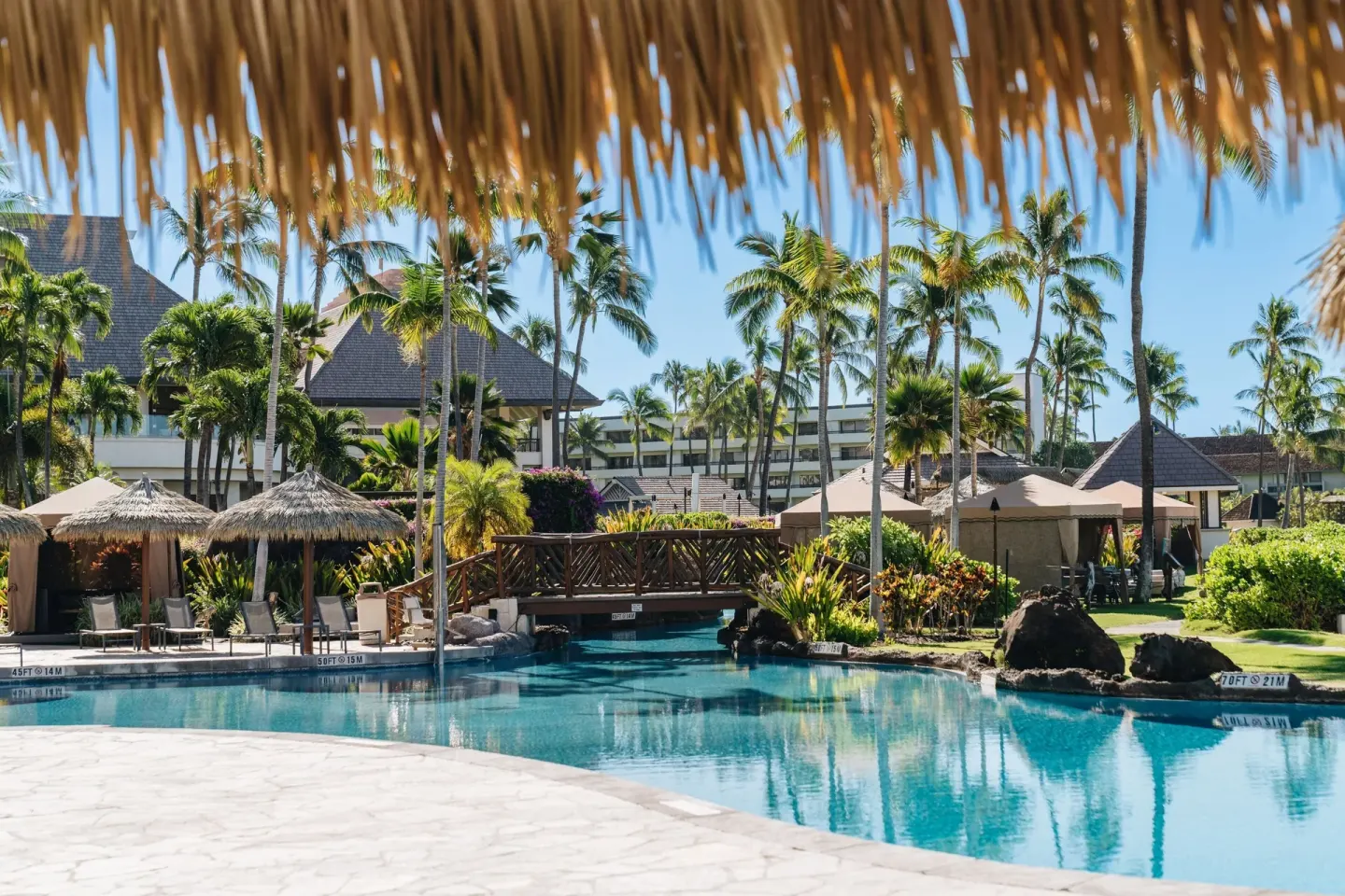 Pool and garden bridge seen beneath a thatched shade at Sheraton Maui Resort & Spa.