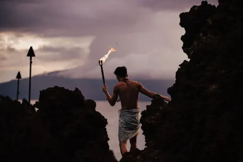 Torch bearer walking through black lava rocks at Sheraton Maui Resort & Spa.
