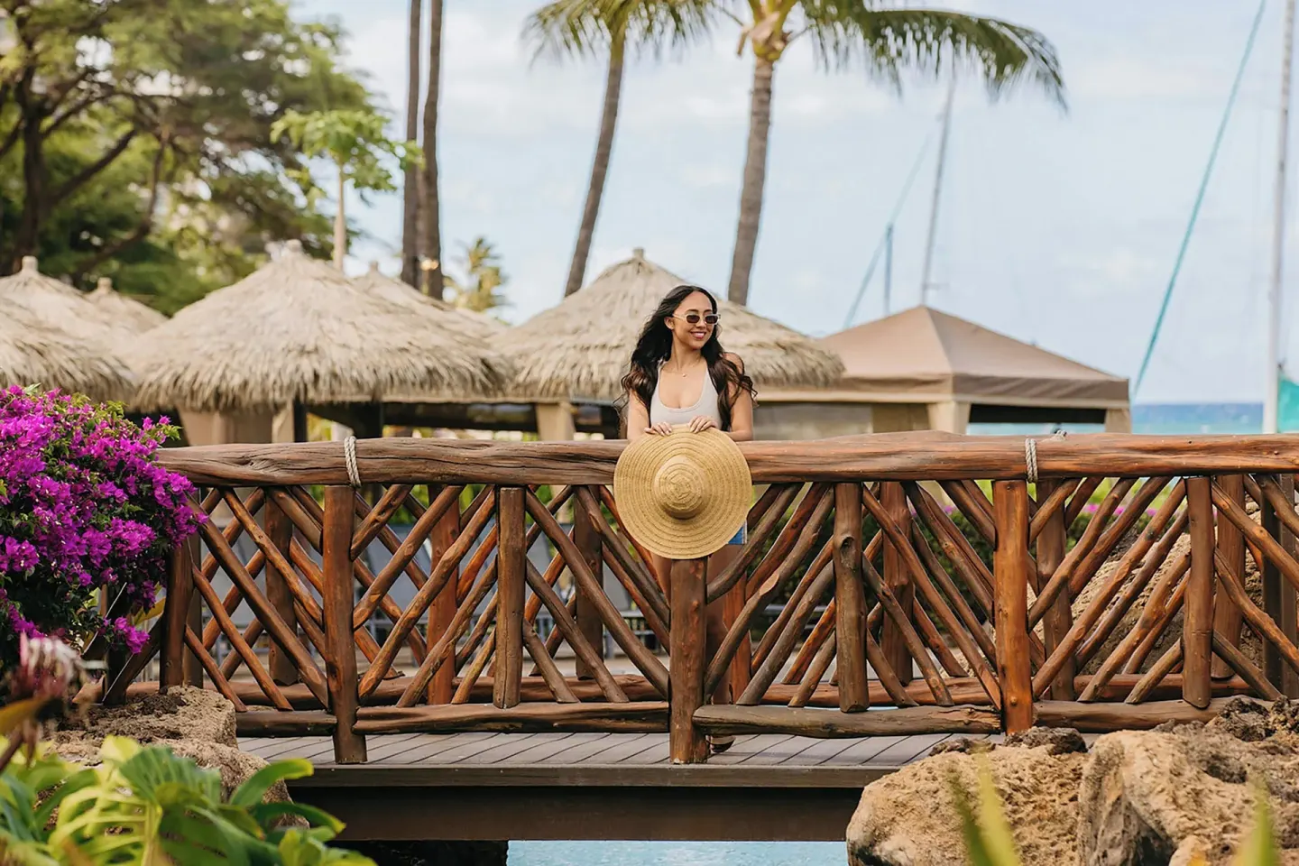 Guest on a wooden bridge by palms and thatched umbrellas at Sheraton Maui Resort & Spa.