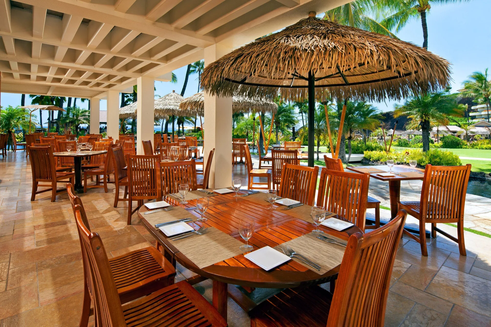 Open-air dining terrace with wood tables and thatched umbrellas at Sheraton Maui Resort & Spa.