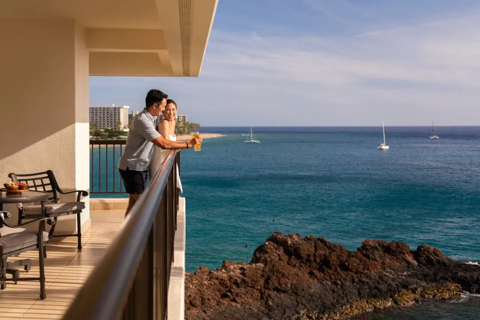 Couple on the oceanfront suite balcony at Sheraton Maui Resort & Spa overlooking the water.