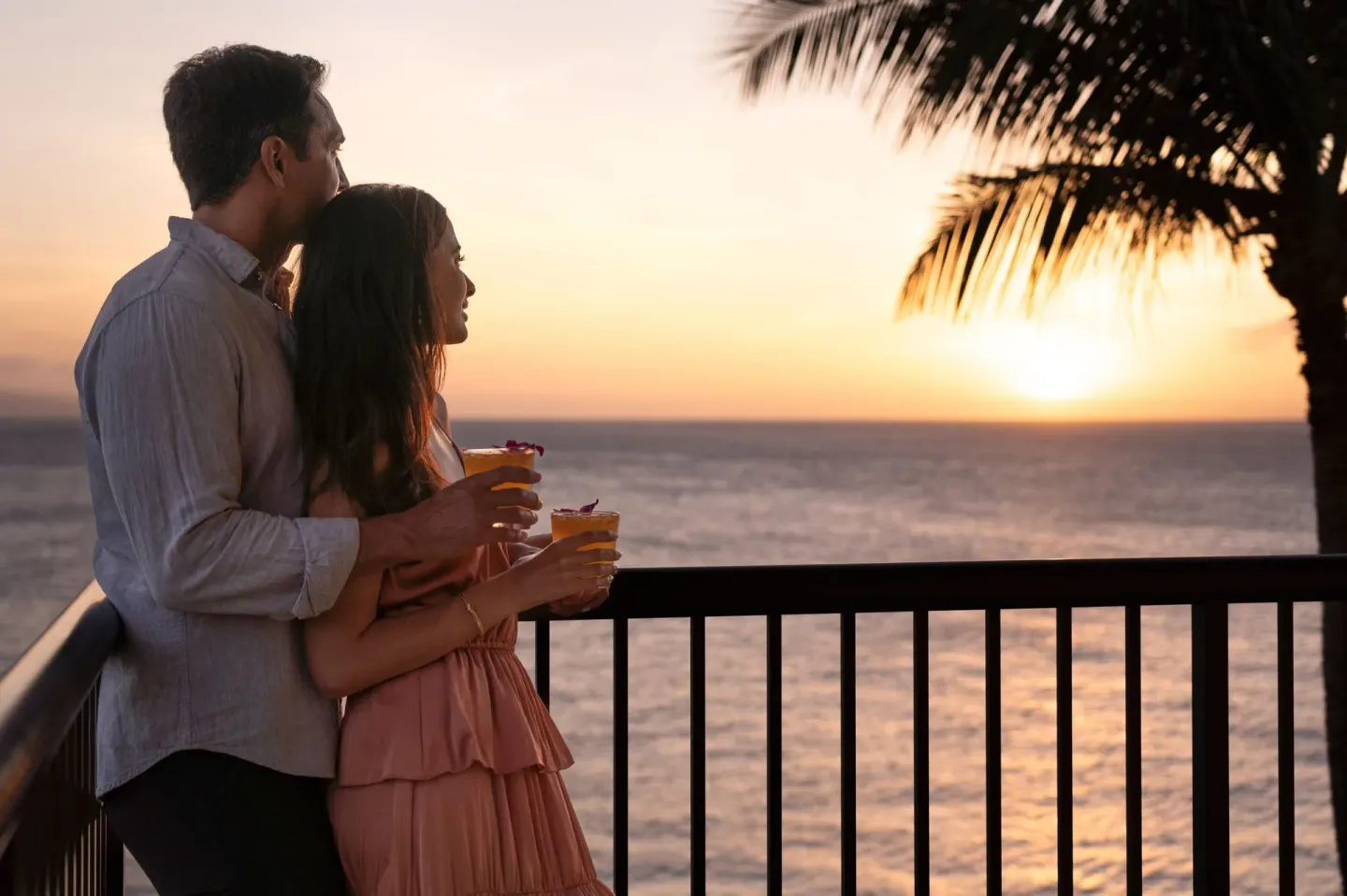 Couple holding drinks on an oceanfront balcony at Sheraton Maui Resort & Spa.