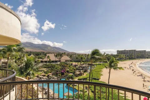 Beachfront suite balcony view of the beach, pool, palms, and mountains at Sheraton Maui Resort & Spa.