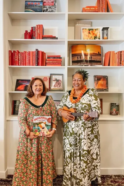 Two women pose with a ukulele and children’s book by shelves at Sheraton Princess Kaiulani.