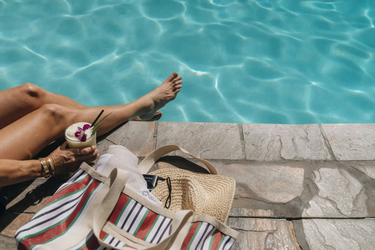 Guest lounges at the pool edge with a drink and striped tote at Sheraton Princess Kaiulani.