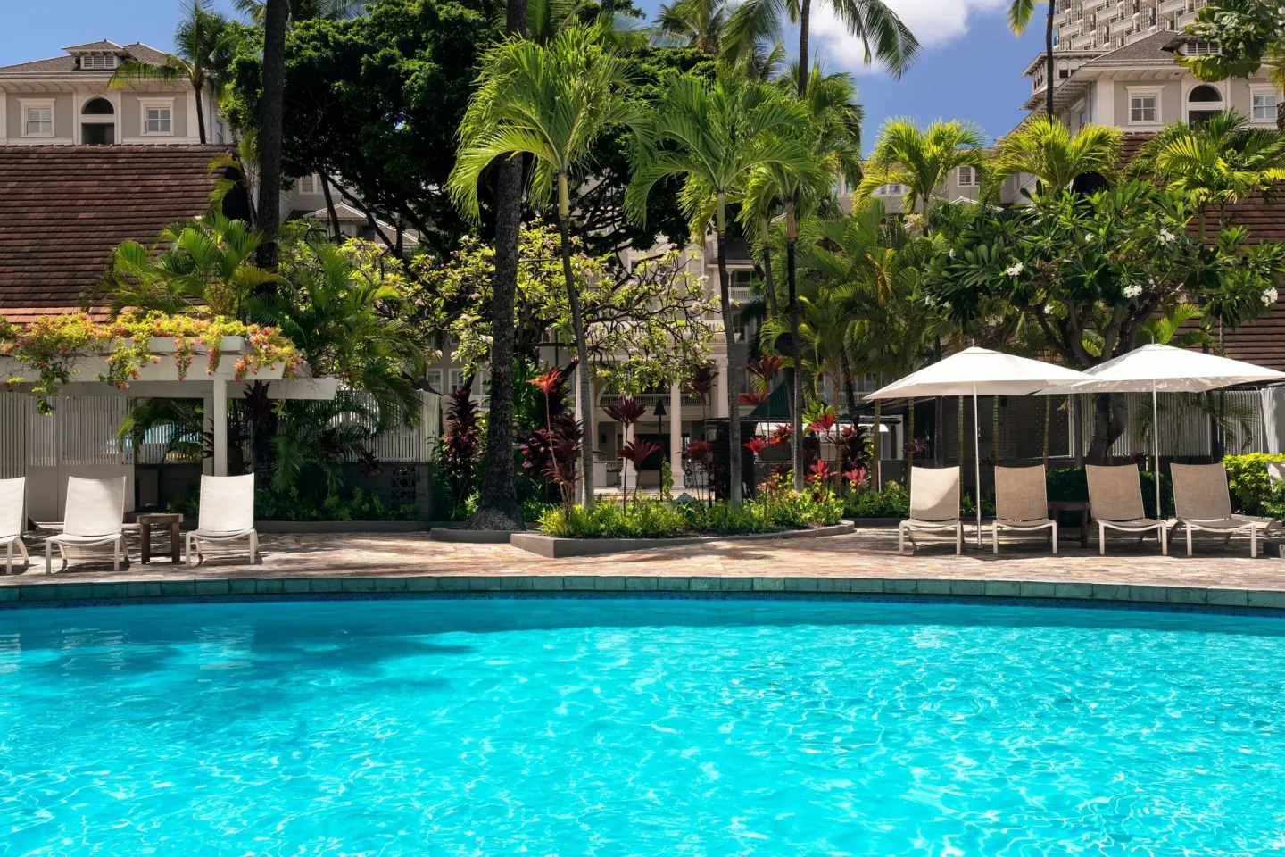 Pool with lounge chairs, umbrellas, palms, and resort buildings at Sheraton Princess Kaiulani.