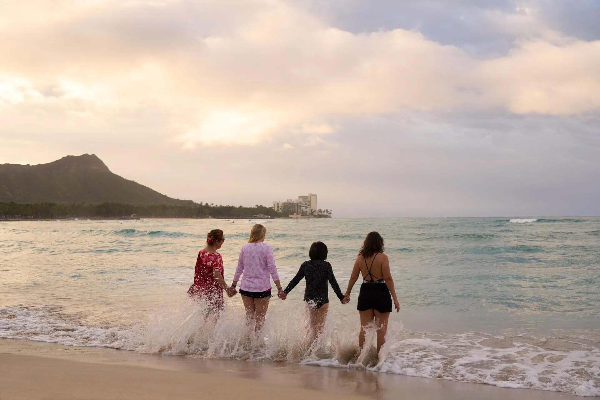 Four people wade into the surf near Sheraton Princess Kaiulani at sunset.