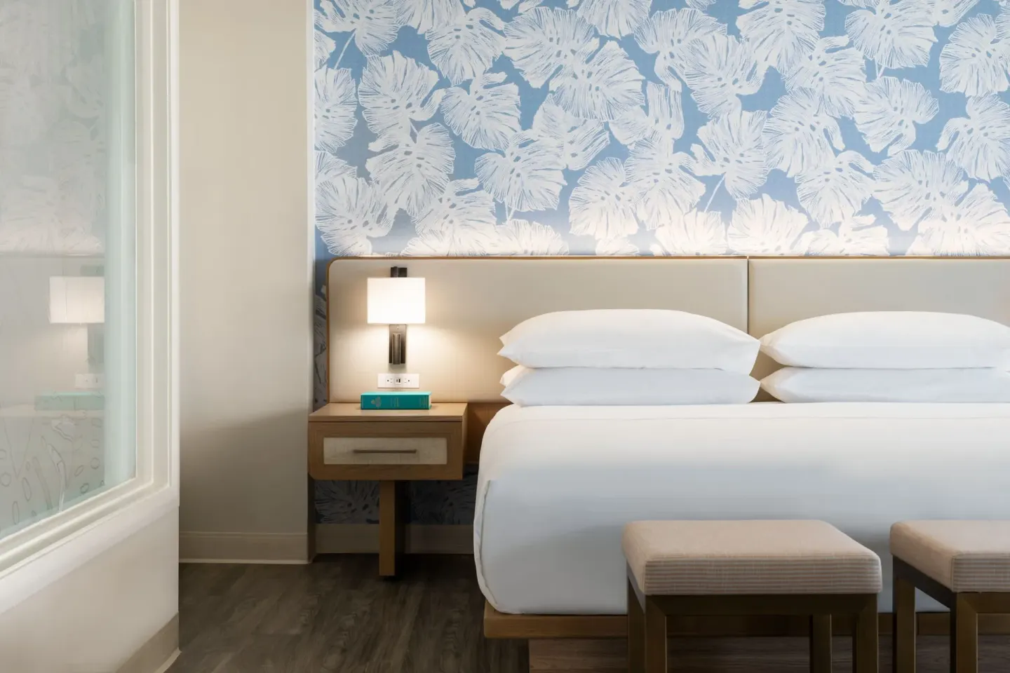 Renovated Corner Jr. Suite king bed at Sheraton Princess Kaiulani with floral wall covering and bedside lamp.