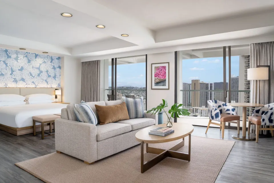 Renovated Corner Jr. Suite living and king bed area at Sheraton Princess Kaiulani with balcony views.