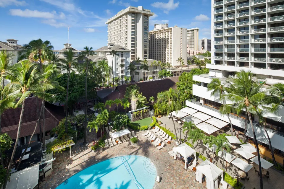 Pool view from a Sheraton Princess Kaiulani guest room with palms, loungers, and Waikiki towers.