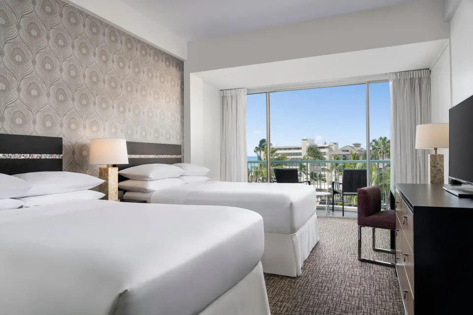 Two queen beds in a Pool View room at Sheraton Princess Kaiulani with balcony beyond.