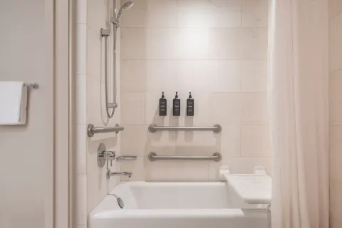Accessible bathtub with grab bars, shower wand, curtain, and bath amenities at Sheraton Waikiki Beach Resort.