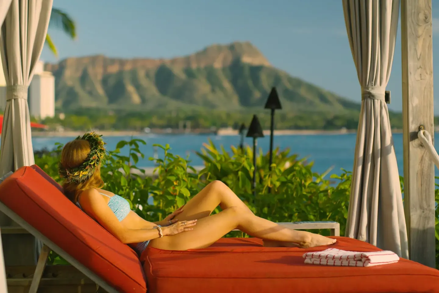 Guest reclining on a red cabana daybed with Diamond Head beyond at Sheraton Waikiki Beach Resort.