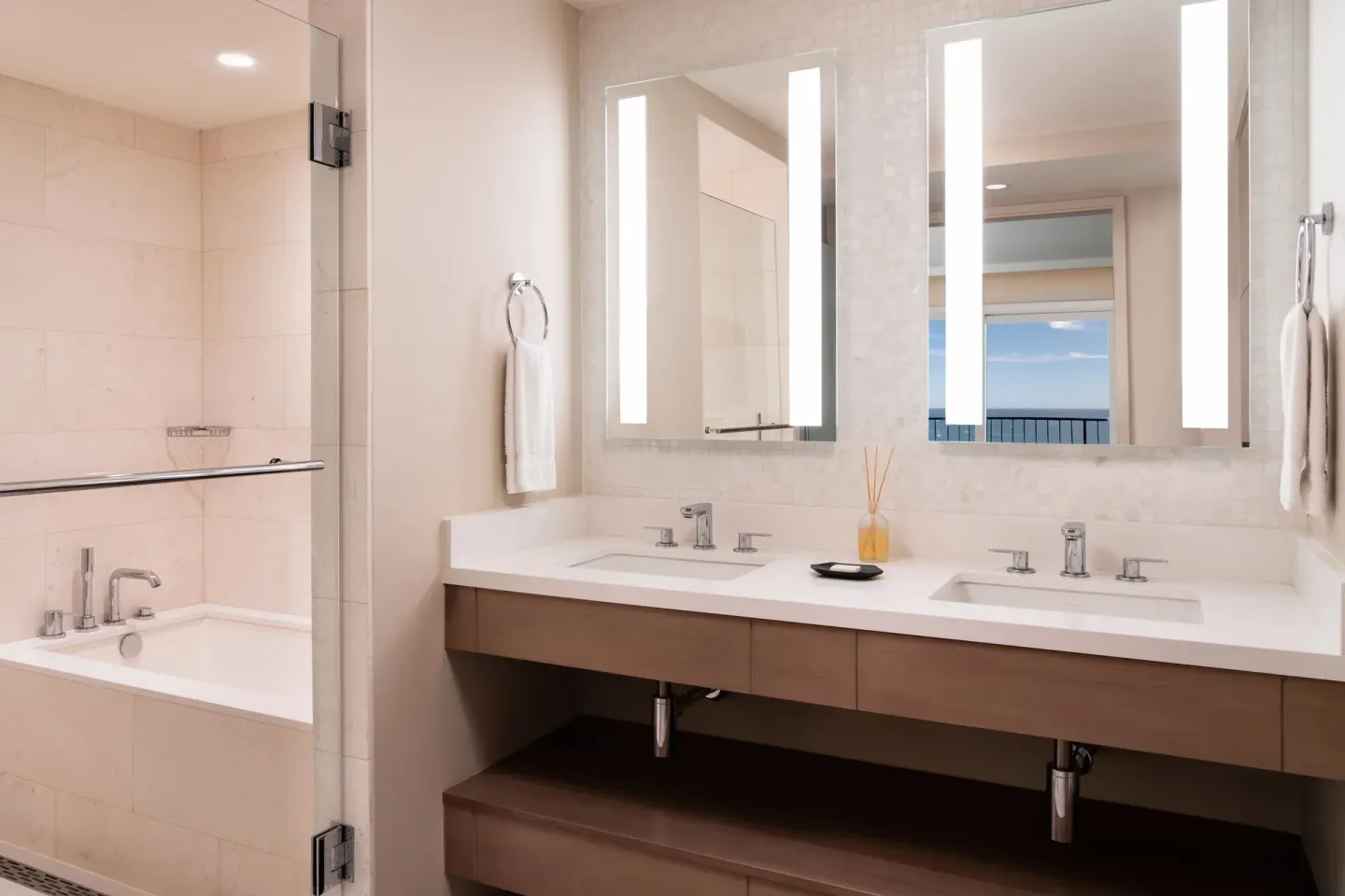 Bathroom with double vanity, lit mirrors, tub, and ocean glimpse at Sheraton Waikiki Beach Resort.
