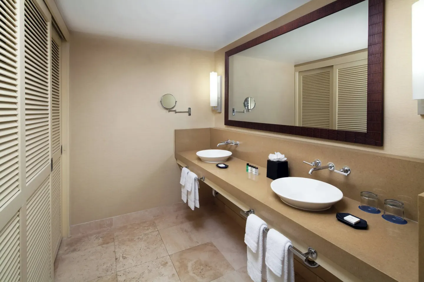 Bathroom with twin vessel sinks, long mirror, towels, and louvered closet doors at Sheraton Waikiki Beach Resort.