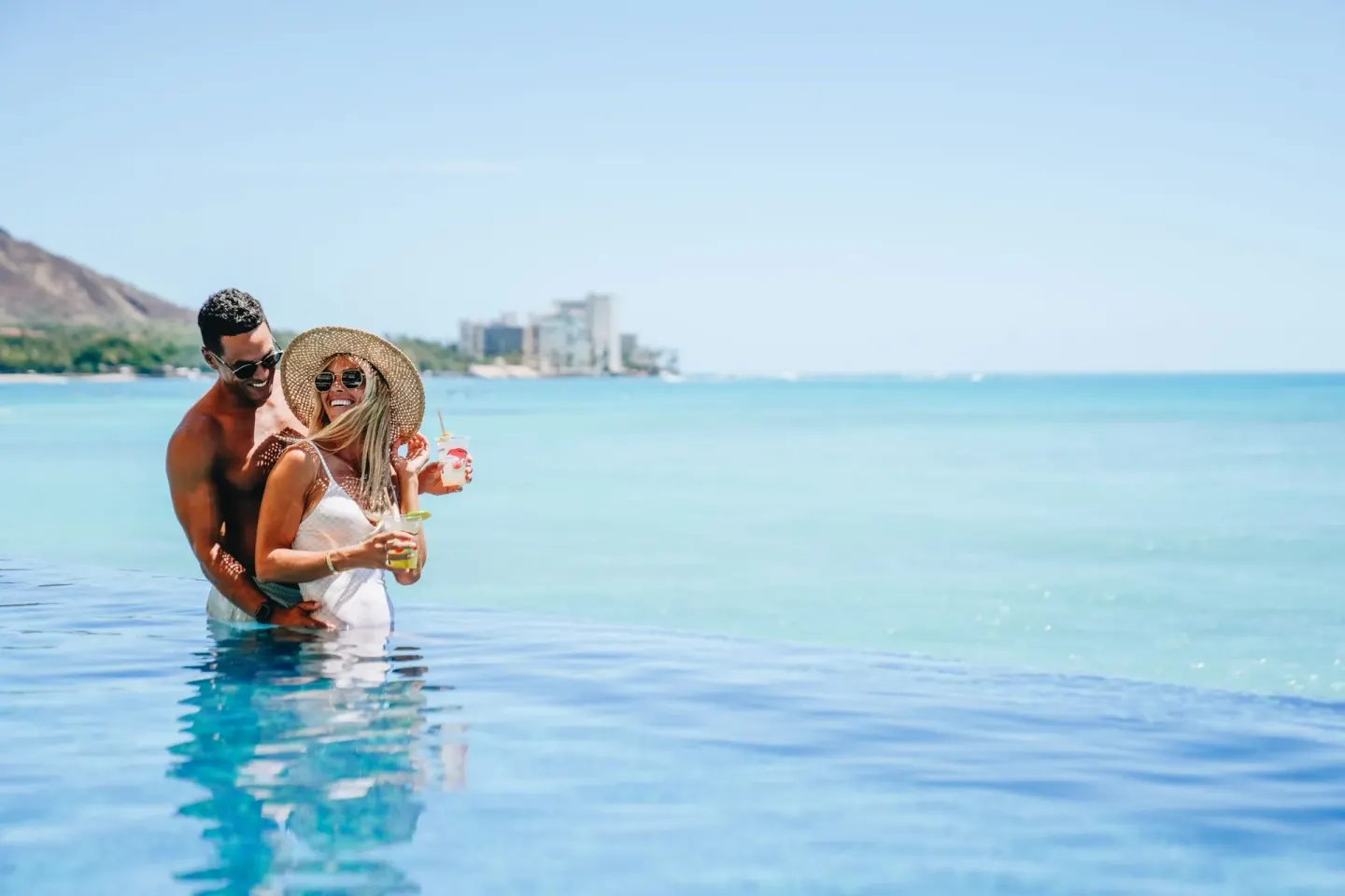 A couple holds drinks in an infinity pool at Sheraton Waikiki Beach Resort.