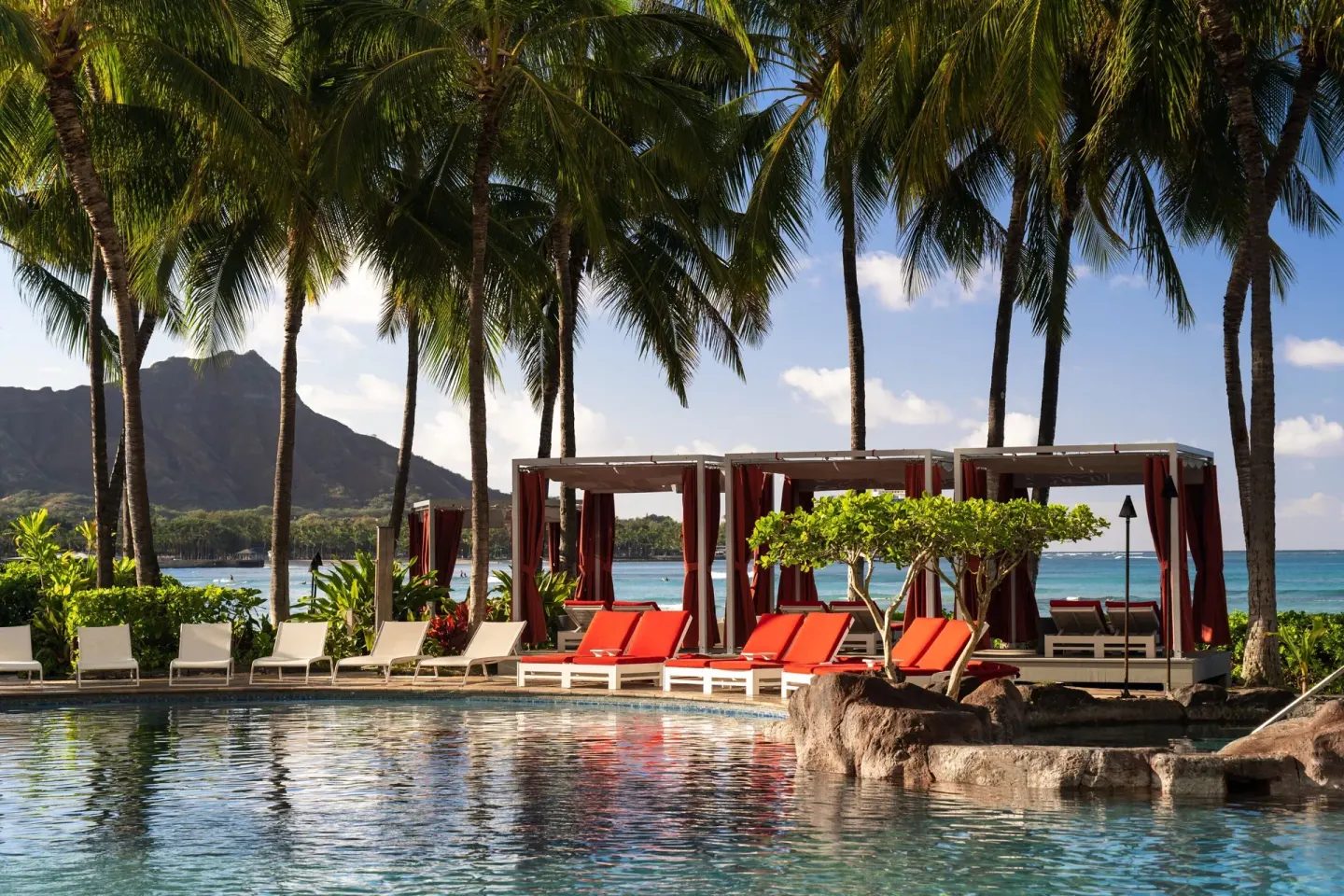Poolside loungers and cabanas under palms near Diamond Head at Sheraton Waikiki Beach Resort.