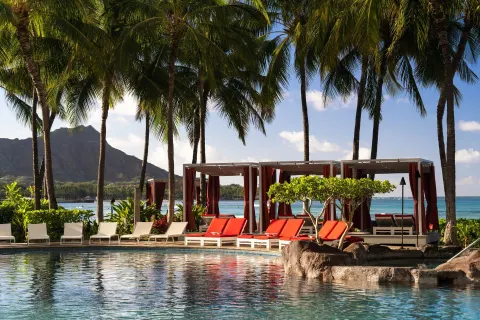 Poolside loungers and cabanas under palms near Diamond Head at Sheraton Waikiki Beach Resort.