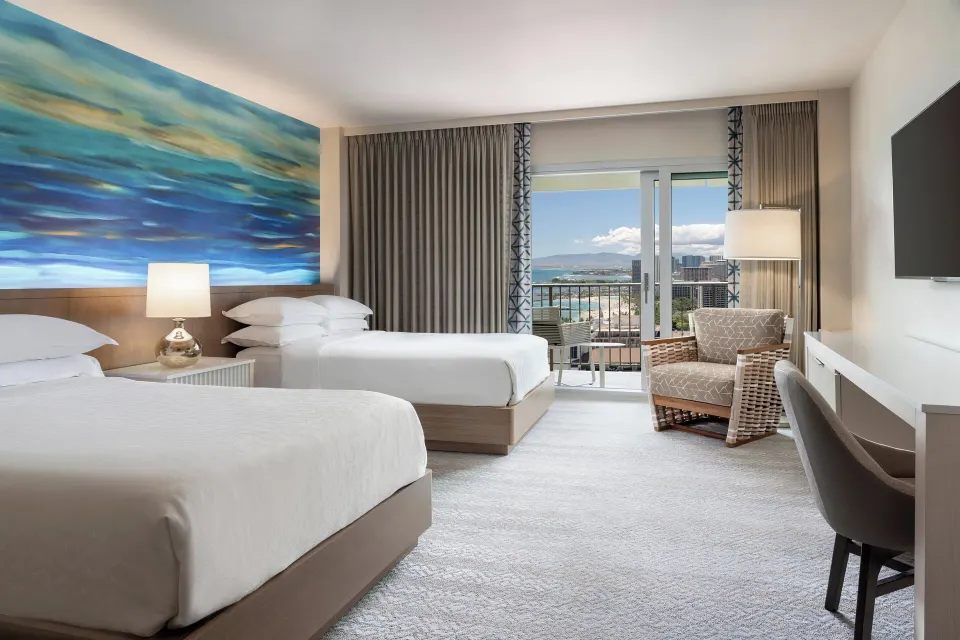 Two-bed guest room with balcony and partial ocean view at Sheraton Waikiki Beach Resort.