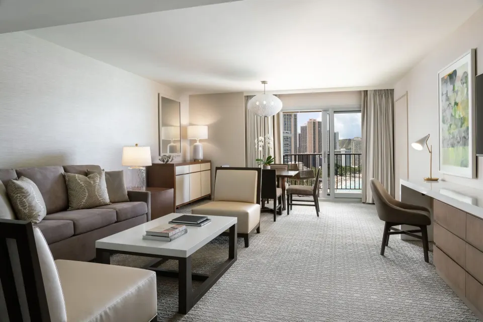 Malia Suite living room with sofa, desk, dining table, and balcony at Sheraton Waikiki Beach Resort.