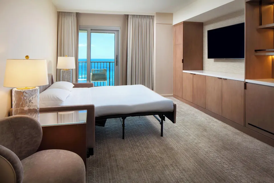 Living area sleeper sofa and ocean-facing balcony at Sheraton Waikiki Beach Resort.