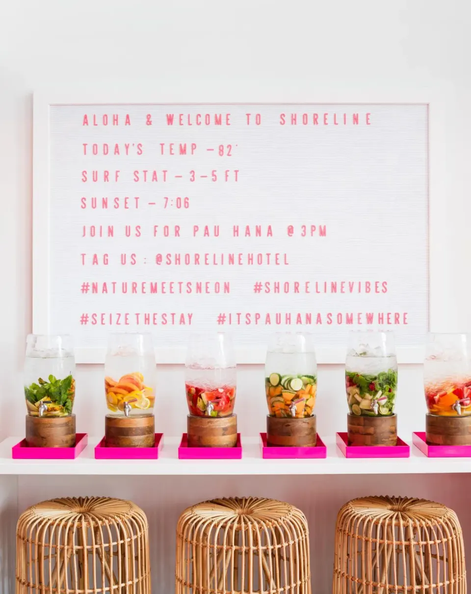 Welcome sign, fruit-infused drink dispensers, and rattan stools at Shoreline Hotel Waikiki.