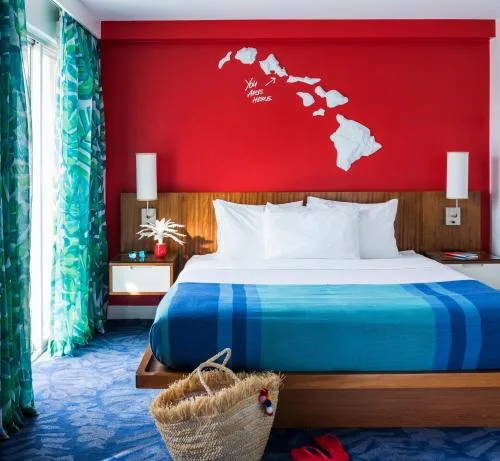 One-bed guest room with tropical curtains and red wall at Shoreline Hotel Waikiki.