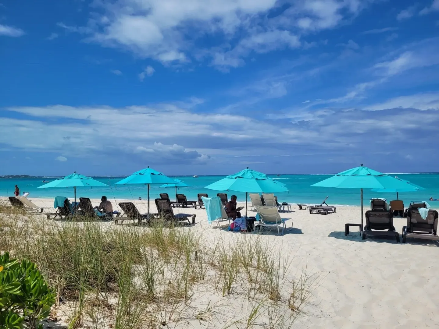 Beach loungers and turquoise umbrellas beside clear water at Sibonné Beach Hotel.