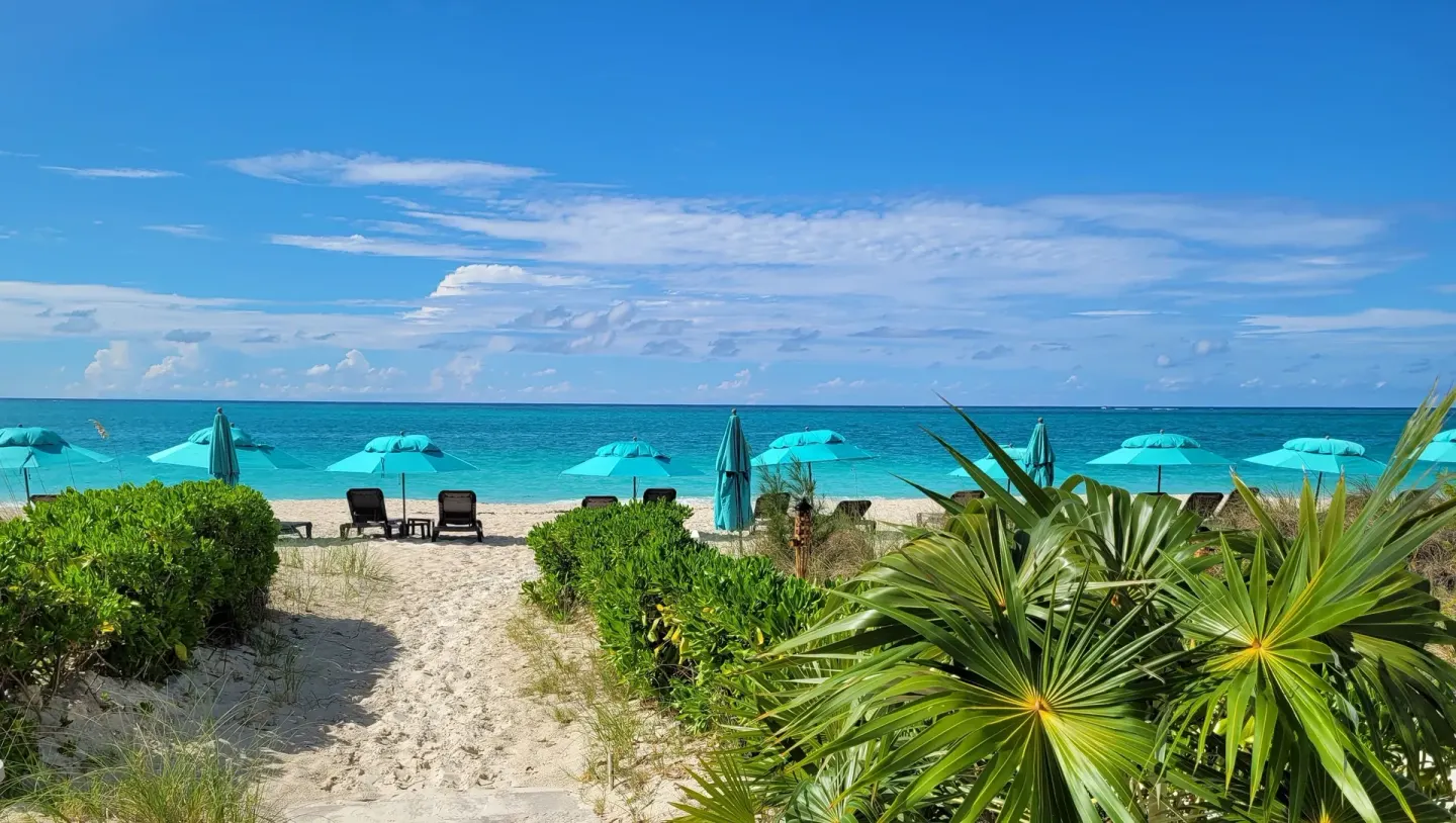 Beach path with turquoise umbrellas and ocean at Sibonné Beach Hotel.
