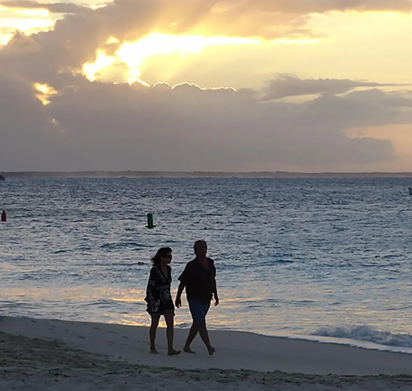 Two people walk along the beach at sunset by Sibonné Beach Hotel.