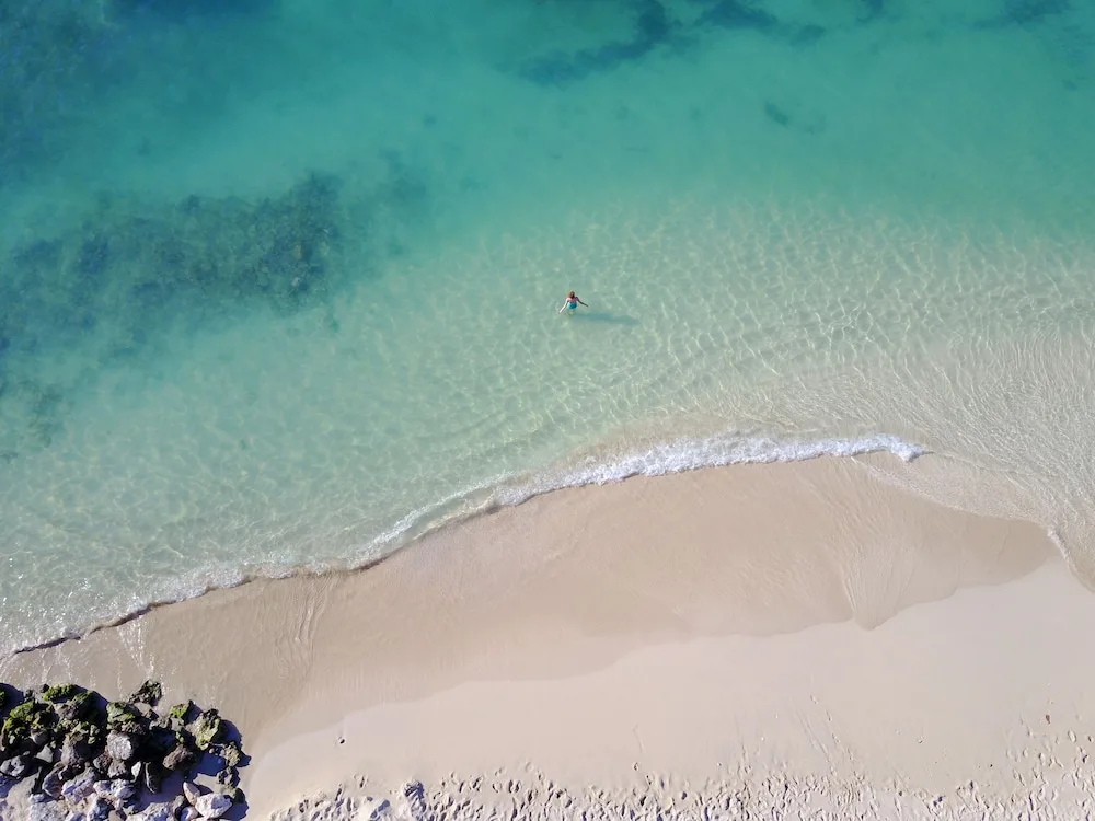 Aerial beach view at Simpson Bay Resort, Marina & Spa with clear water, pale sand, and one swimmer.